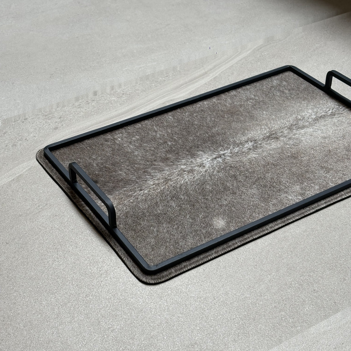 Charola cowhide grande - 319, vista cerca. Piel natural gris con matices claros y herrería negra.