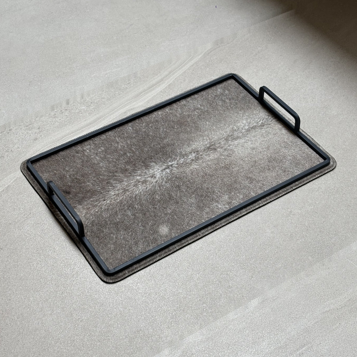 Charola cowhide grande - 319, vista lejos. Piel natural gris con matices claros y herrería negra.