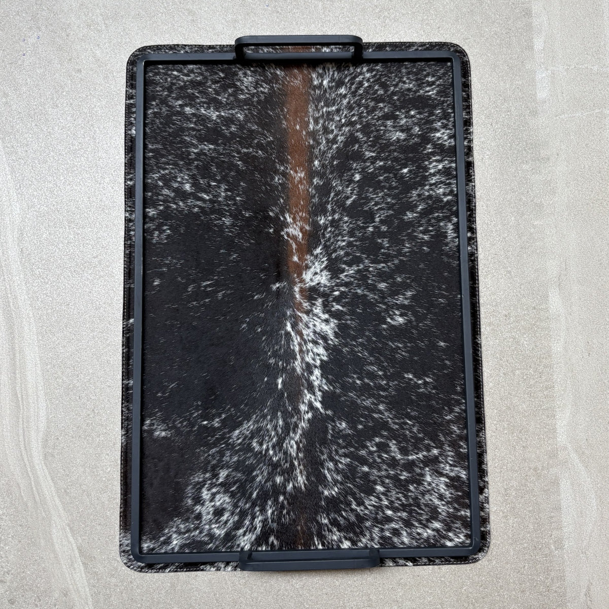 Charola cowhide grande - 325, vista superior. Piel natural negro con blanco y café y herrería negra.