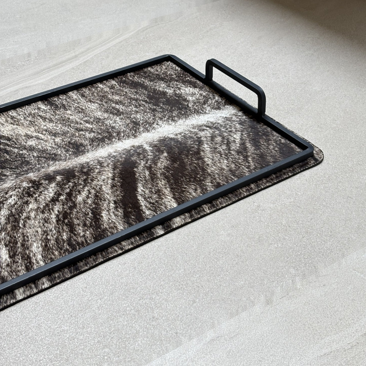 Charola cowhide grande - 326, vista cerca. Piel natural café atigrado con blanco y herrería negra.