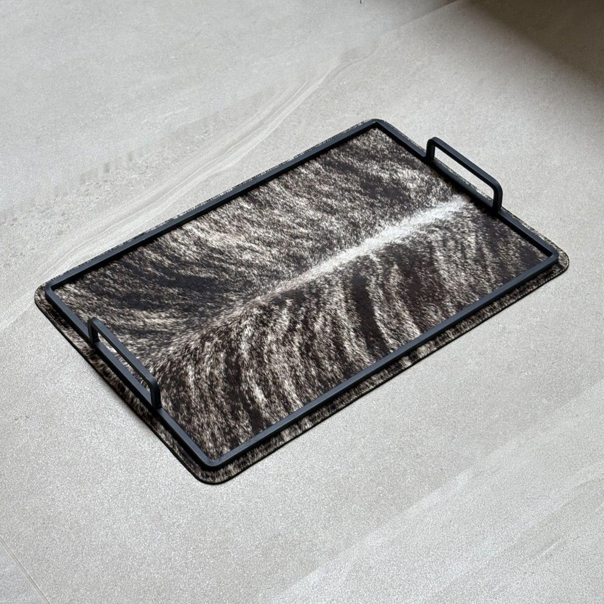 Charola cowhide grande - 326, vista lejos. Piel natural café atigrado con blanco y herrería negra.