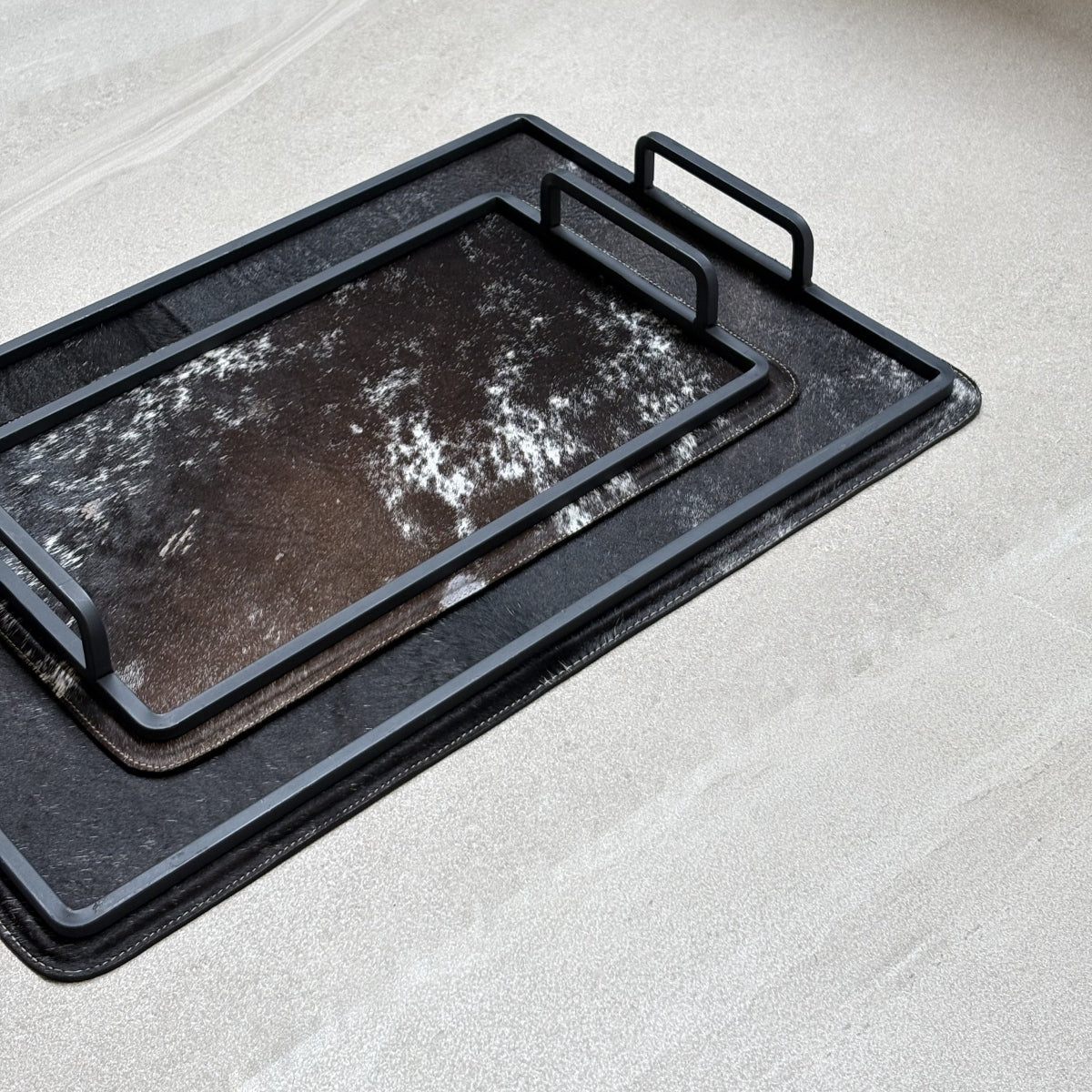 Set de charolas cowhide - 310, vista cerca. Piel natural negro y café con blanco y herrería negra.